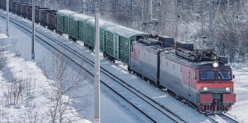 Red electric locomotive hauls freight wagons along snow-covered railway tracks in winter