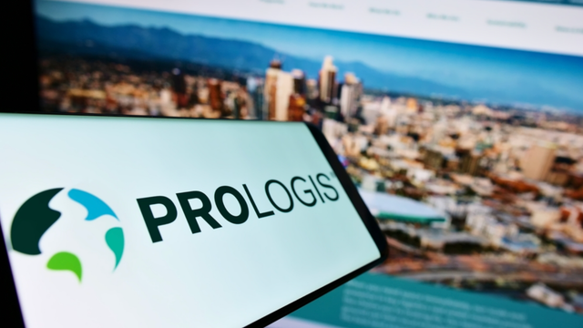 Smartphone showing the Prologis logo held in front of a screen displaying a city skyline