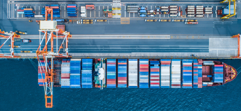 Overhead aerial photo of a container ship moored alongside a terminal quay, with a gantry crane and container yard above it.