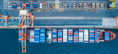 Overhead aerial photo of a container ship moored alongside a terminal quay, with a gantry crane and container yard above it.