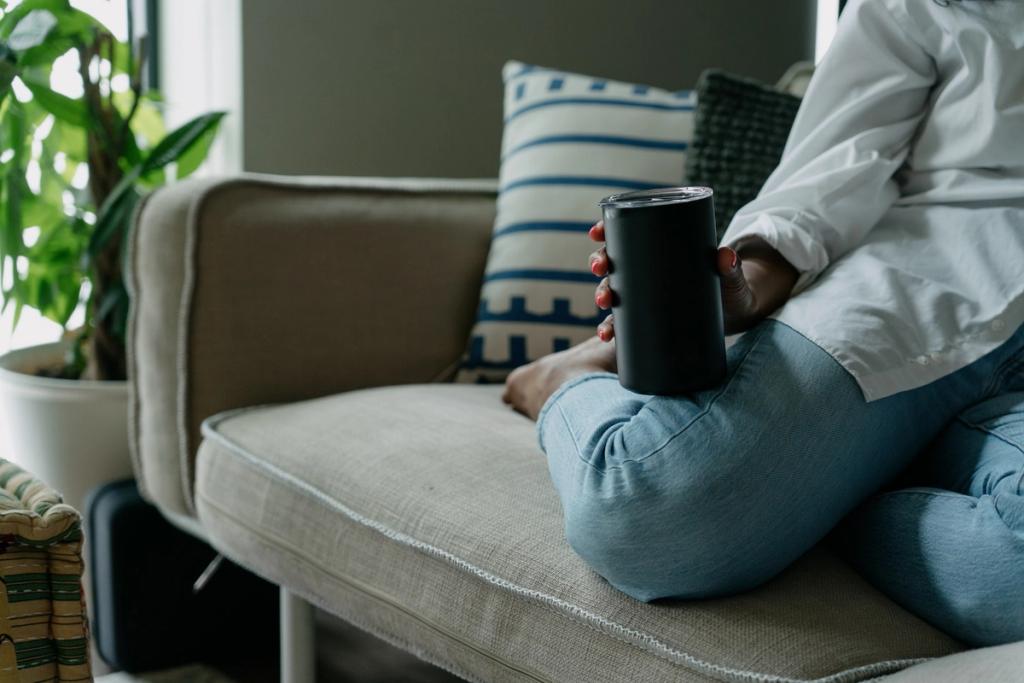 Person seated on a couch holding a black insulated tumbler with red nail polish