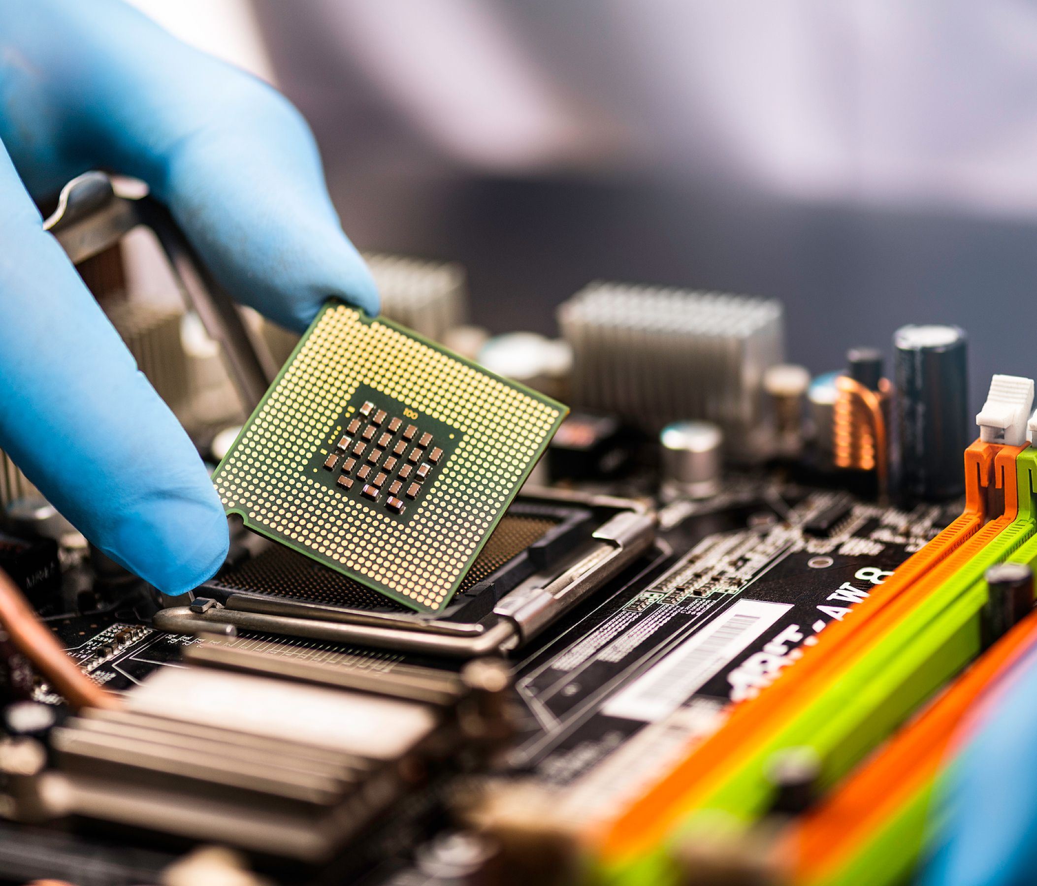 Gloved hand seating a CPU chip into a motherboard socket on an electronics assembly line