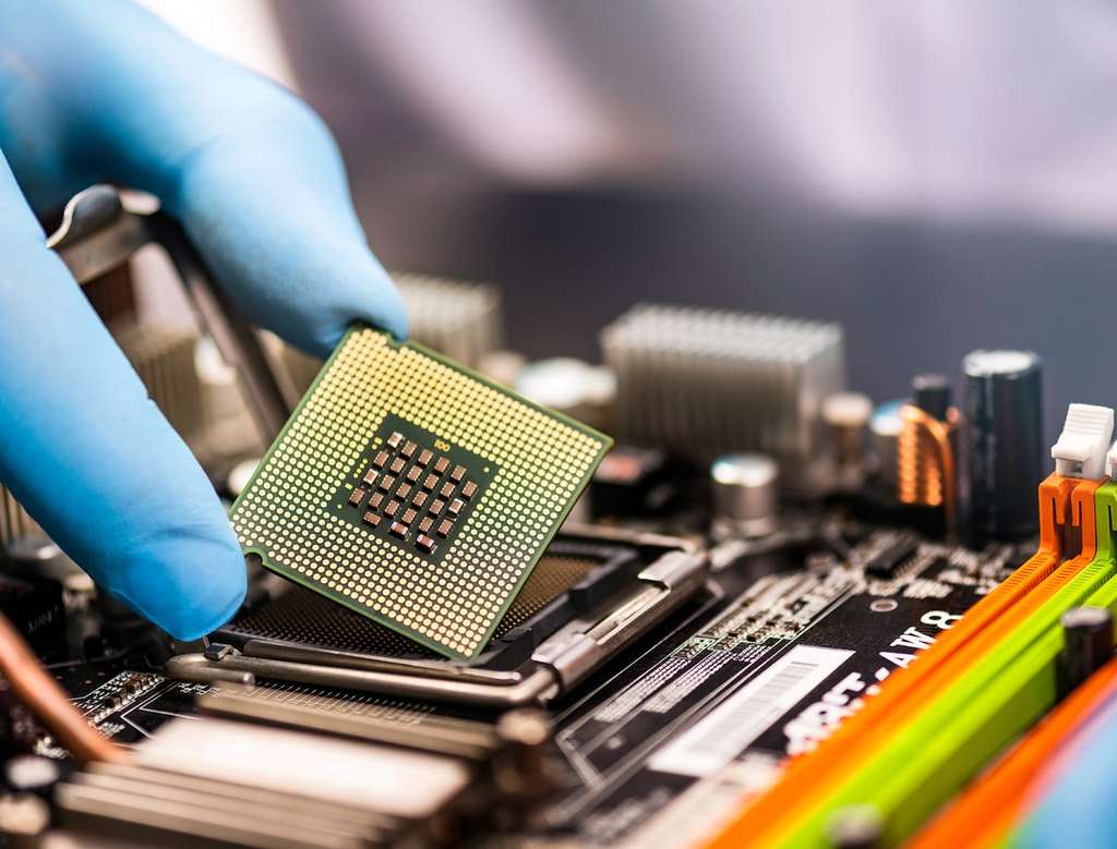 Gloved hand seating a CPU chip into a motherboard socket on an electronics assembly line