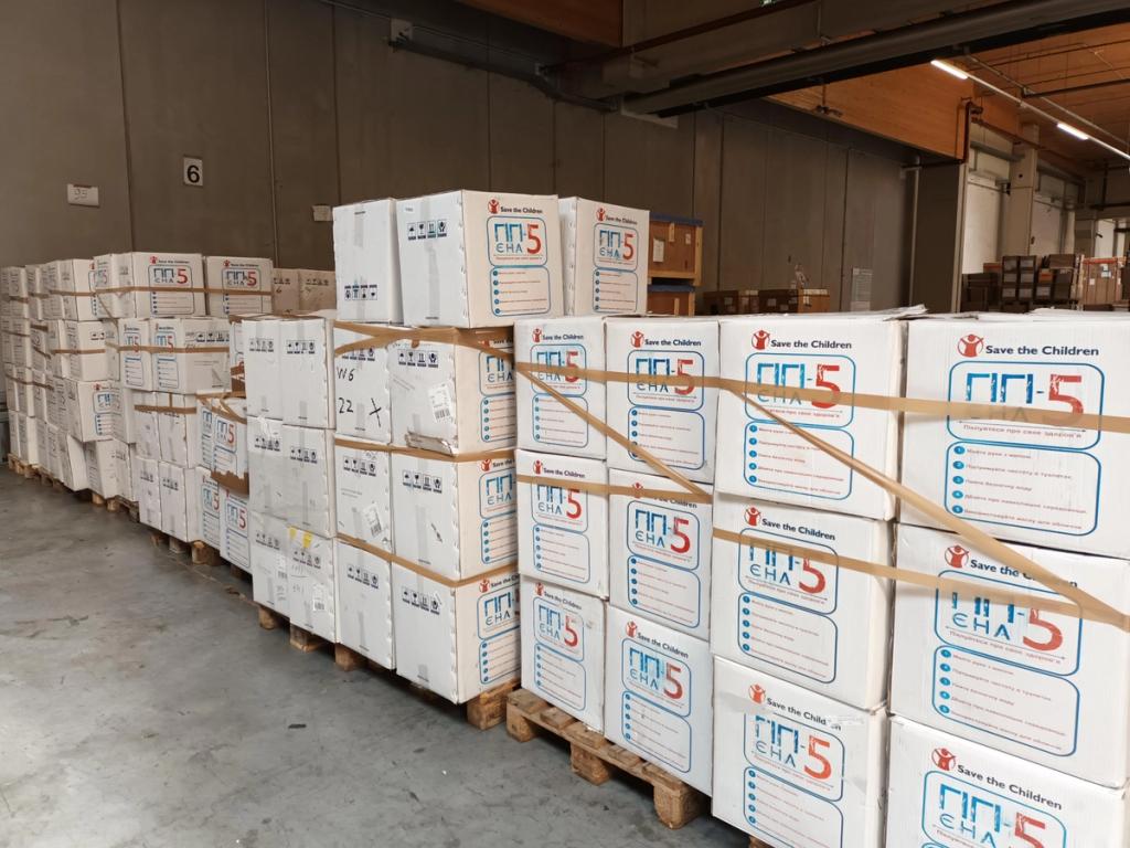 Pallets of stacked Save the Children aid boxes in a warehouse