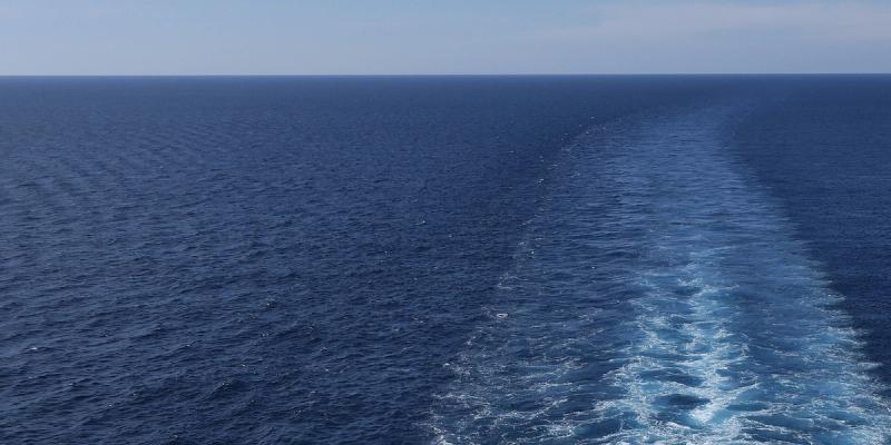 Open blue ocean with a ship's frothy wake trailing across the horizon