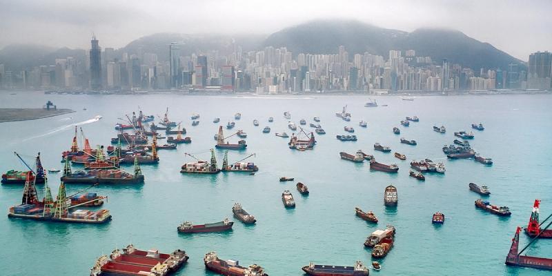 Hazy view of Hong Kong harbor with barges and cargo boats before a skyline and mountains