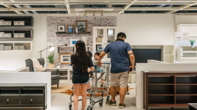 A family with two children walks through a furniture showroom past sofas, beds and home decor displays