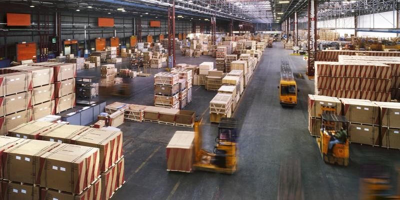 Elevated view of a large warehouse interior with crated freight and yellow forklifts in motion