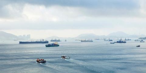 Cargo ships and tugboats anchored in a misty harbor with hills in the background