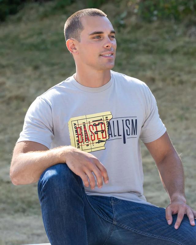 Young man in a Baseballism graphic t-shirt and jeans seated outdoors