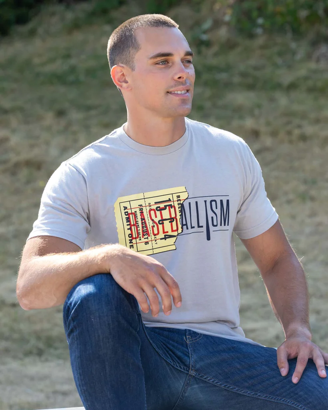 Young man in a Baseballism graphic t-shirt and jeans seated outdoors