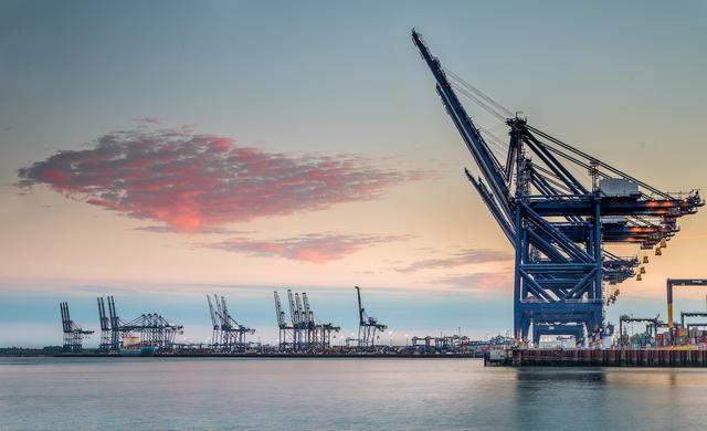 Container port at dusk with tall ship-to-shore gantry cranes along the waterfront under a pink and blue sky