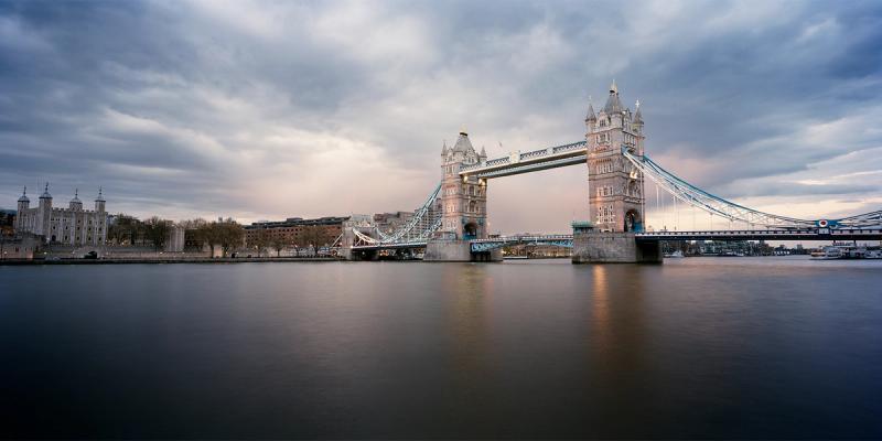 Tower Bridge and the Tower of London across the River Thames under a cloudy sky