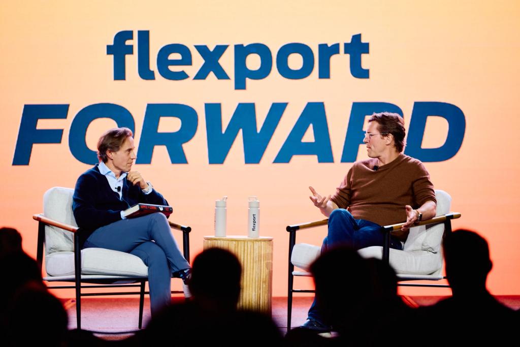 Two men in armchairs talking on stage before a large 'flexport FORWARD' backdrop
