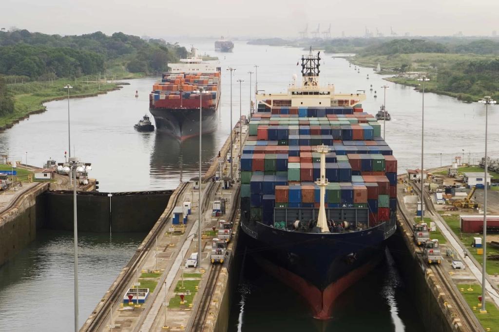 Two container ships pass through parallel lock chambers of the Panama Canal lined with locomotives and lamp posts.