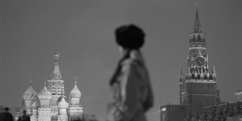 Black-and-white Moscow Red Square scene with blurred figure, St. Basil's domes and the Kremlin Spasskaya clock tower.
