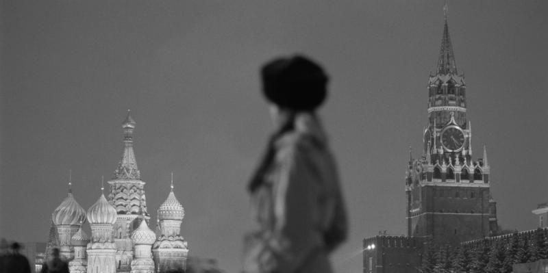 Black-and-white Moscow Red Square scene with blurred figure, St. Basil's domes and the Kremlin Spasskaya clock tower.