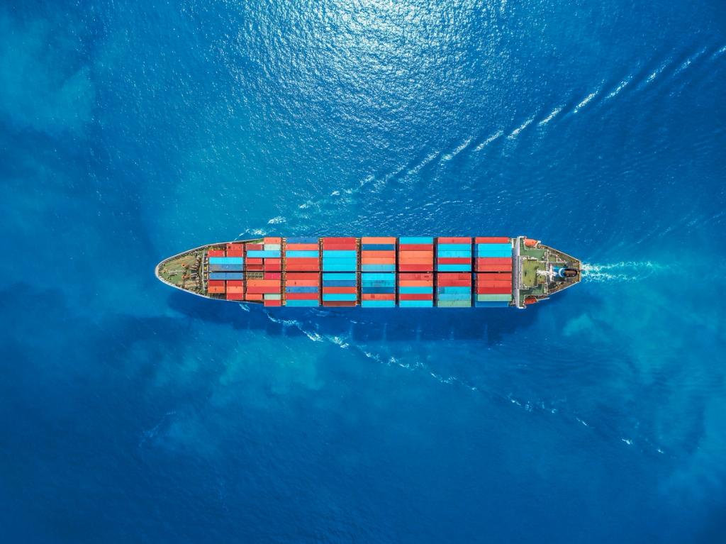 Aerial top-down view of a container ship with red and blue containers underway on deep blue ocean