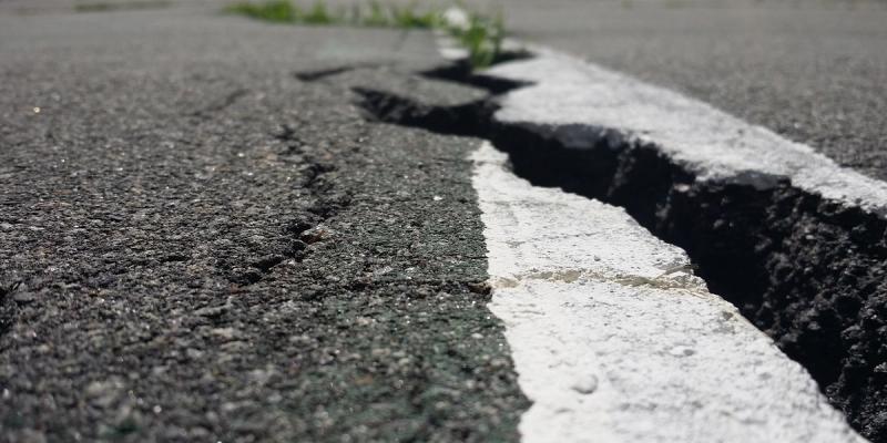 Close-up of a crack splitting a paved road through a white painted line