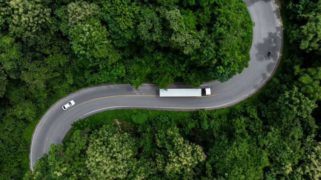 Aerial view of a winding road through a dense forest with vehicles traveling on the highway.