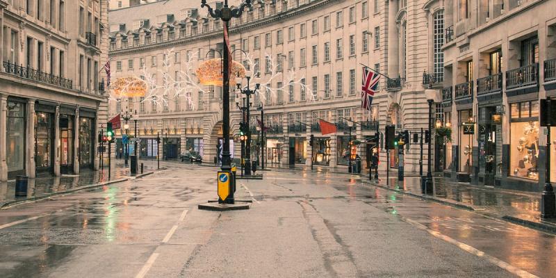 Empty rain-slicked London curved street lined with classical buildings, holiday lights and a Union Jack flag