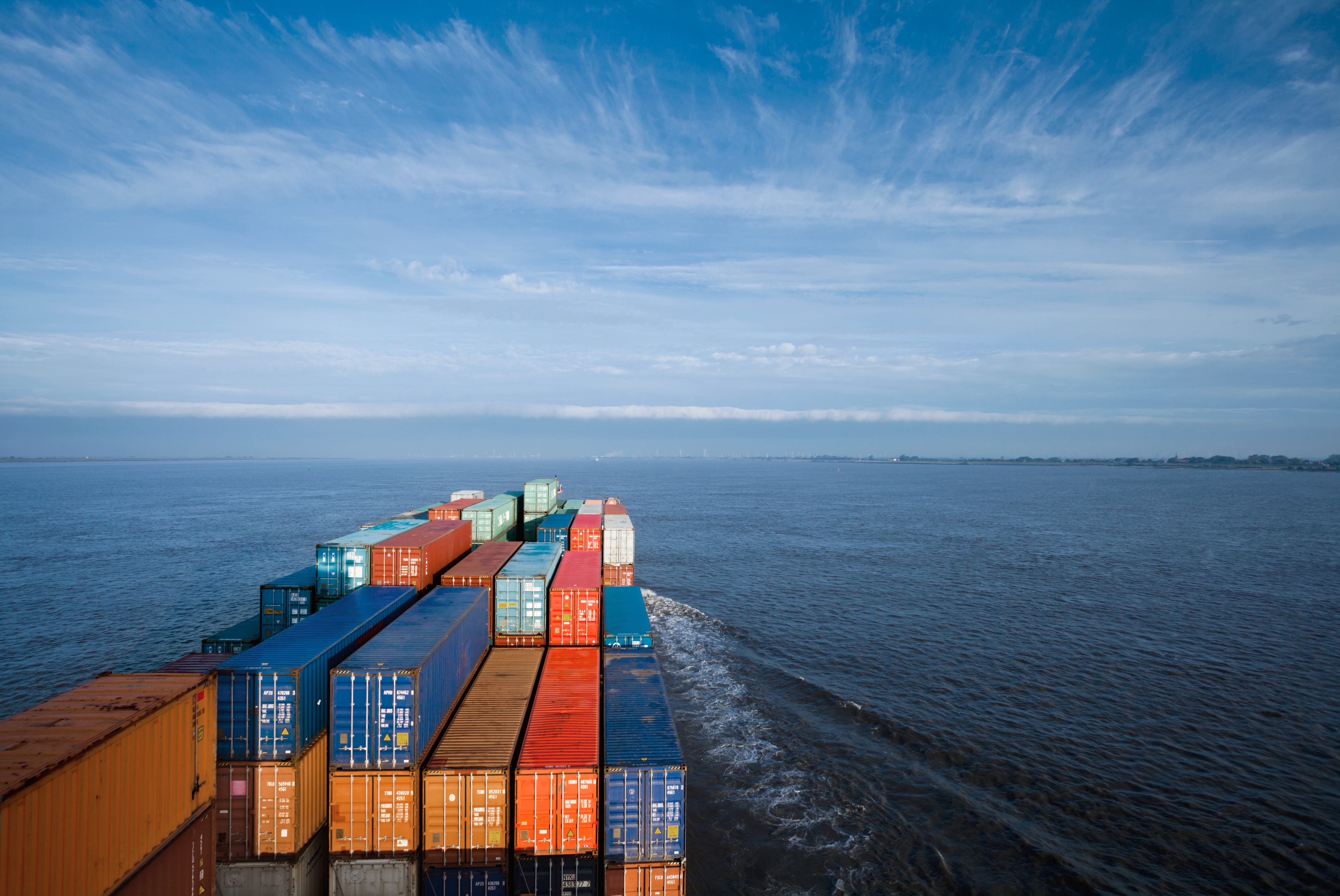 Cargo containers stacked on a cargo ship deck moving across the ocean.