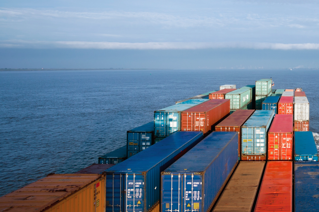 Cargo containers stacked on a cargo ship deck moving across the ocean.