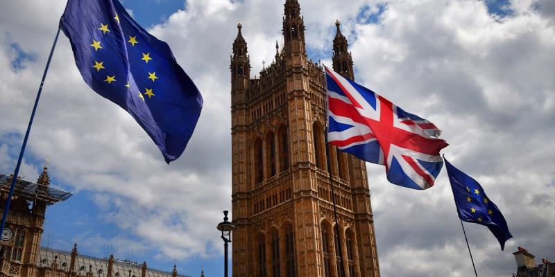 EU and Union Jack flags flying in front of the Houses of Parliament Victoria Tower under a cloudy sky
