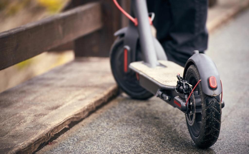 Close-up of a parked black electric scooter on a paved path beside a wooden fence