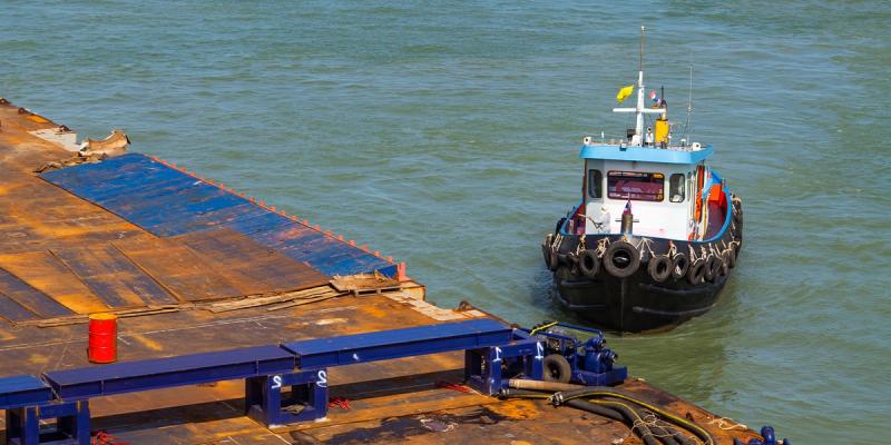 Small tugboat with tire fenders beside a rusty cargo barge on green water