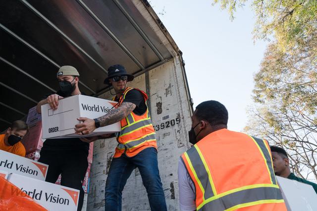 Volunteers in orange safety vests unloading World Vision aid boxes from a truck under trees