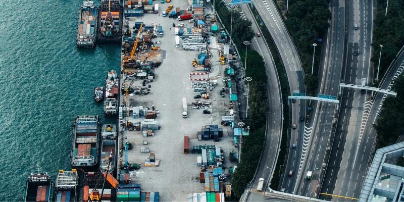 Aerial view of a container port with stacked containers beside a multilane highway