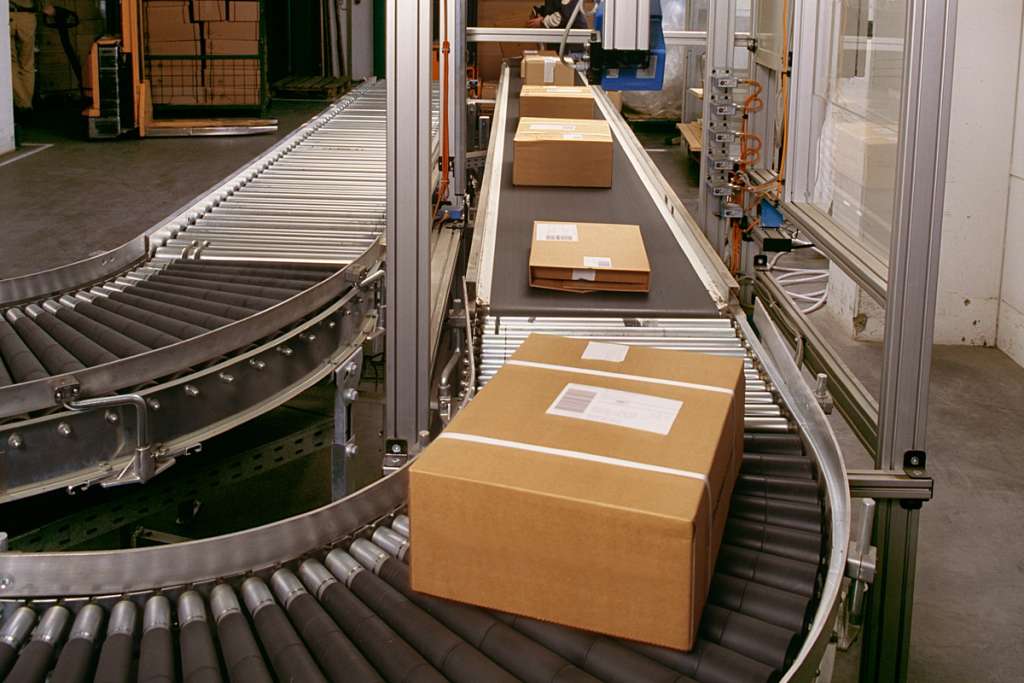 Cardboard boxes moving along a conveyor belt system in a warehouse or distribution facility.
