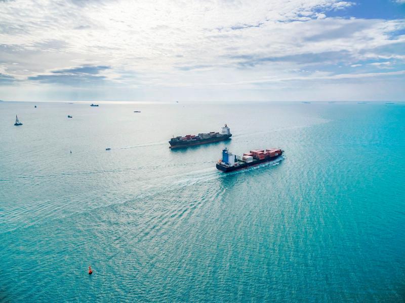 Aerial view of two container ships sailing on calm blue ocean under a cloudy sky