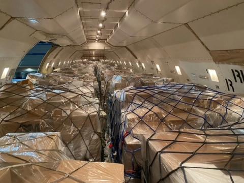 Interior of a cargo aircraft fully loaded with shrink-wrapped pallets secured under cargo nets