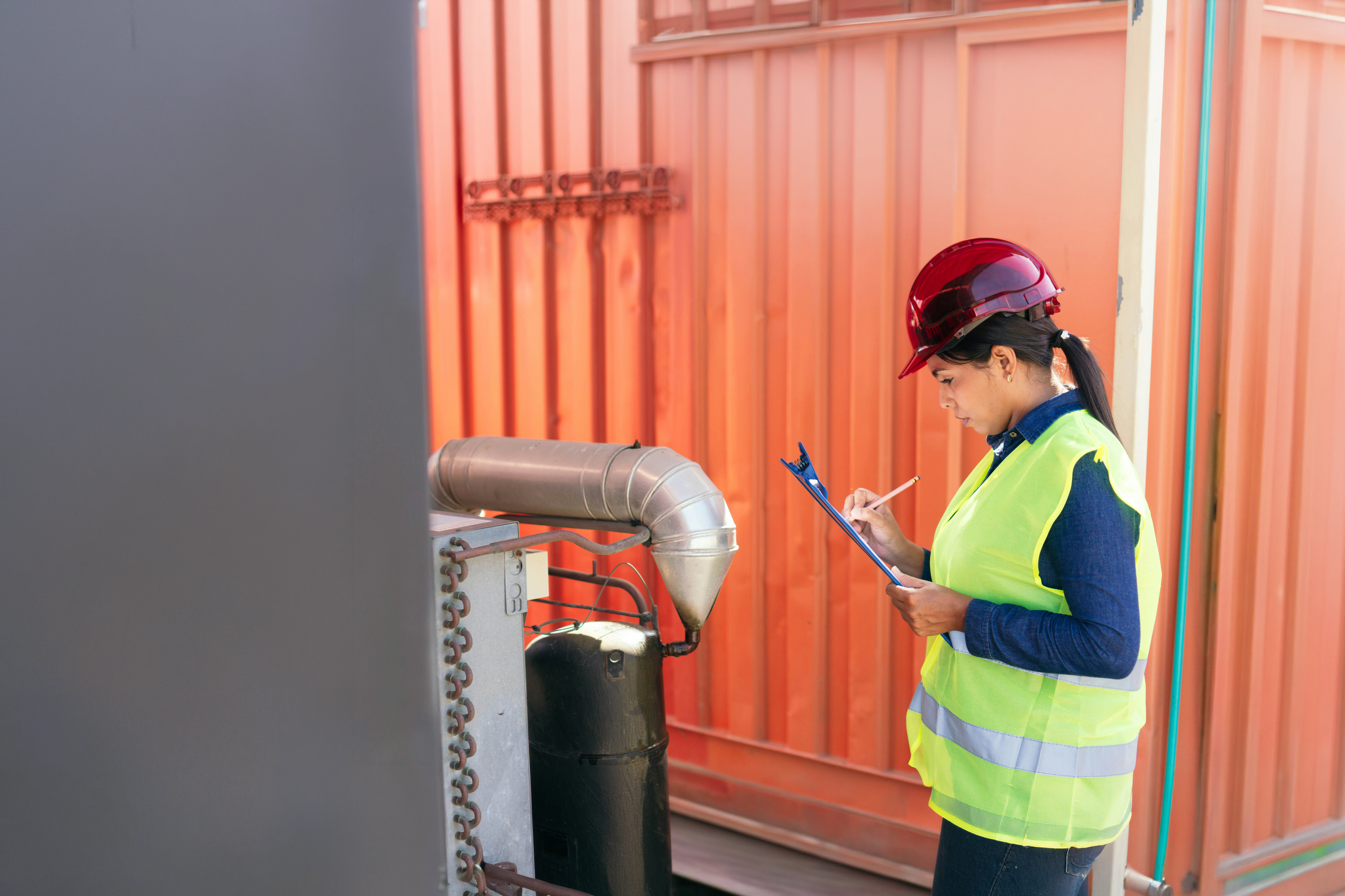 Worker in a hard hat and safety vest opening the door of a shipping container in a container yard.