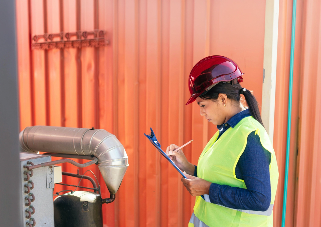 Worker in a hard hat and safety vest opening the door of a shipping container in a container yard.