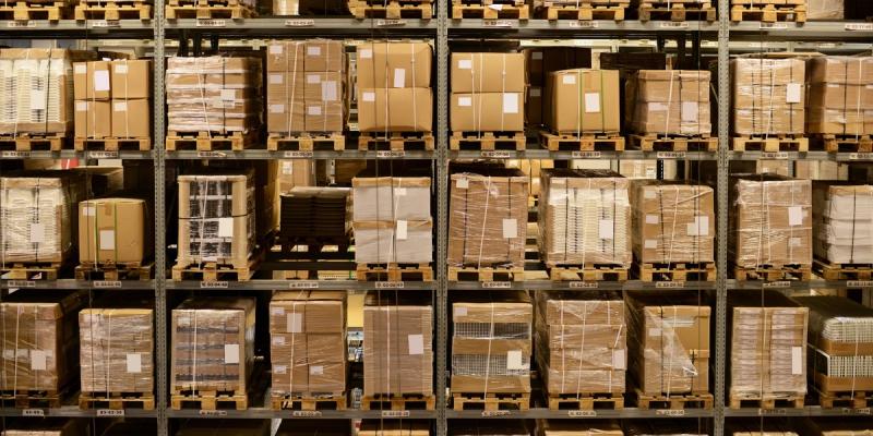 Tall warehouse racks filled with palletized cardboard boxes stacked across multiple shelf levels.