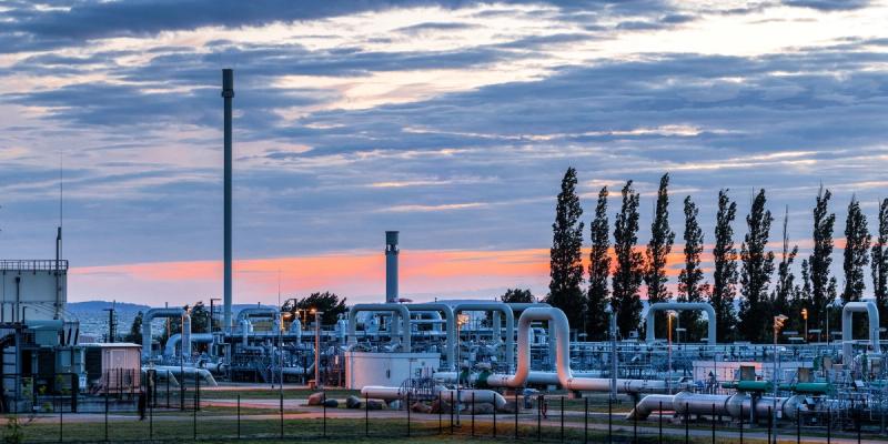 Industrial gas plant with pipelines and tall stacks silhouetted against an orange sunset sky