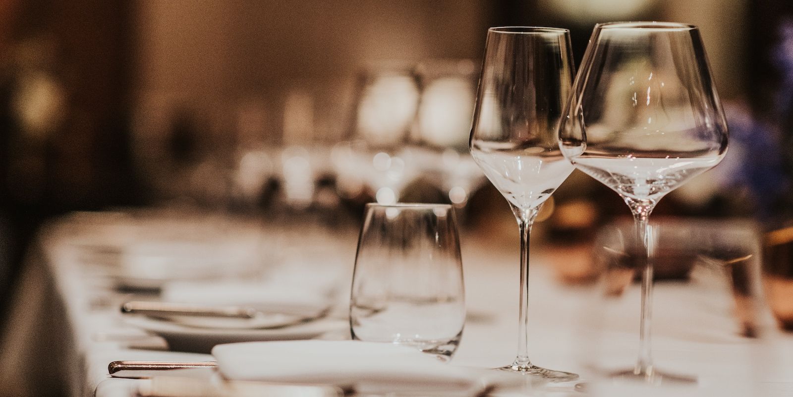 Empty wine and water glasses on a set restaurant table with a softly blurred warm background