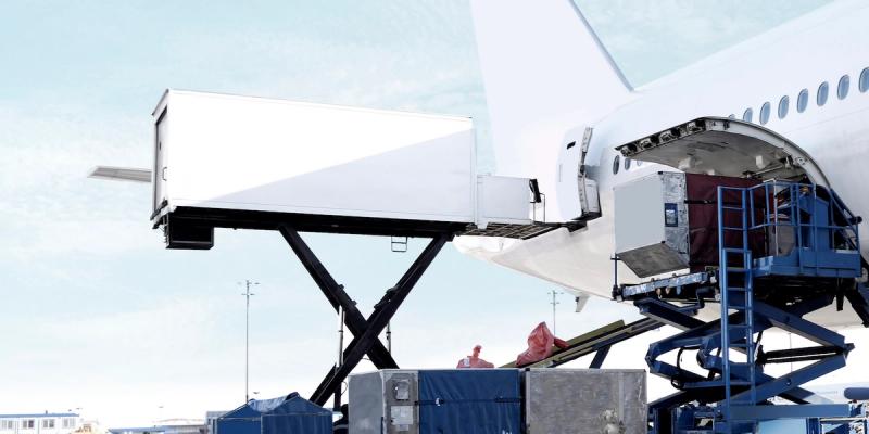Cargo containers being loaded into the hold of a white freighter aircraft on a loading platform