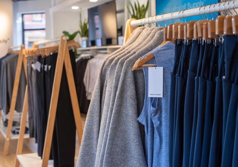 Racks of gray and navy Ministry of Supply apparel displayed in a bright retail store