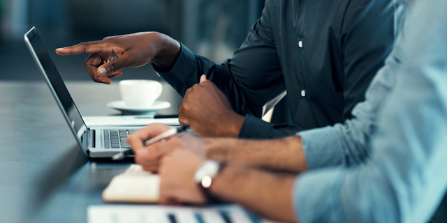 Hands at a desk pointing to a laptop screen while colleagues take notes, evoking a freight forwarding review.