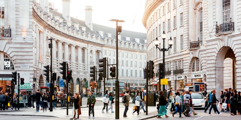 Busy London street at Piccadilly Circus with curved Regent Street facades, traffic lights and pedestrians crossing.
