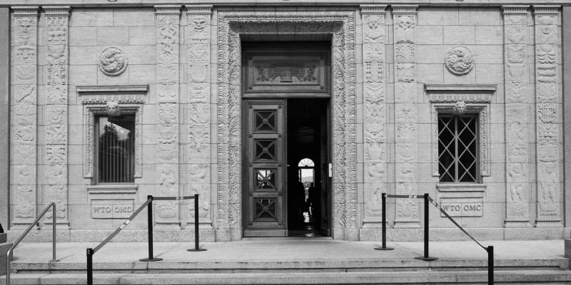 Black-and-white facade of the WTO headquarters with carved stone reliefs and an open bronze door