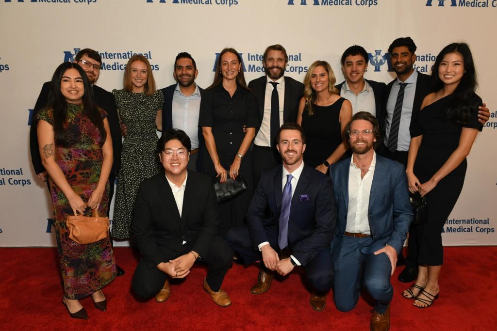Group of people in formal attire pose together on a red carpet before an International Medical Corps step-and-repeat banner.