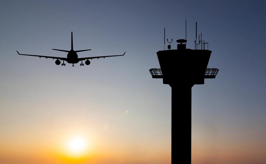 Silhouette of an airplane on final approach past an air traffic control tower at sunset