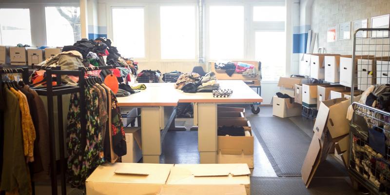 Donation sorting room with clothing on racks and tables and stacks of file boxes