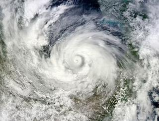 Satellite photo of a large typhoon with a well-defined eye spiraling over the ocean toward a coastline.