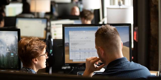 Two colleagues reviewing shipment data together on office monitors in a dim workspace
